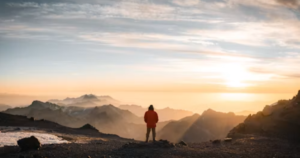 Hiker looking toward a sunrise over mountains, symbolizing confidence and a success mindset