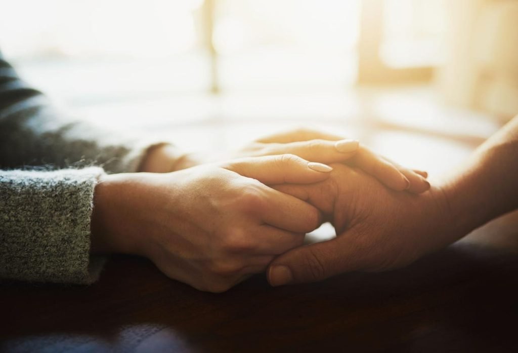 Two people gently holding hands as a symbol of reassurance and emotional support